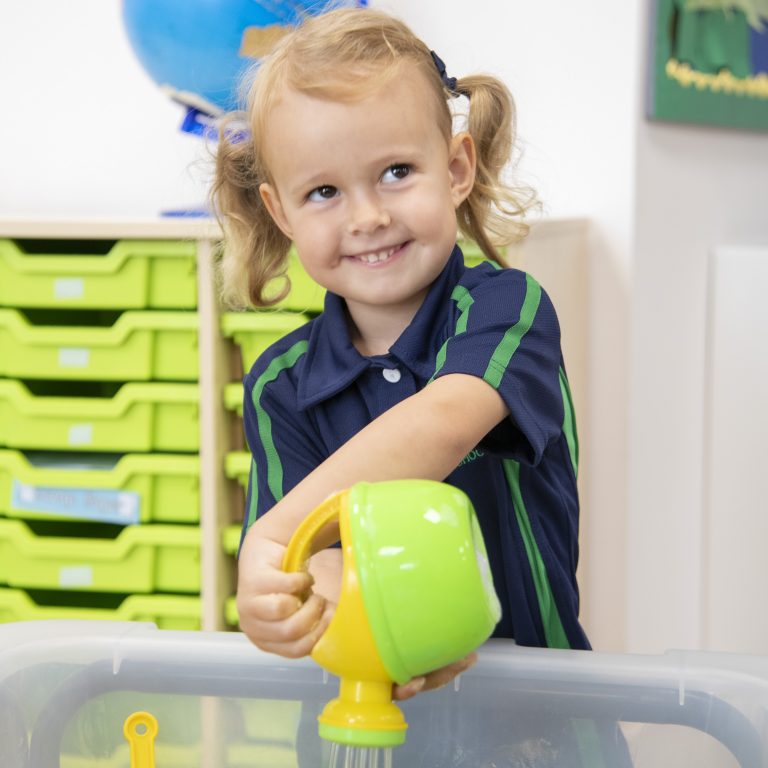 A young school girl playing with a plastic watering can